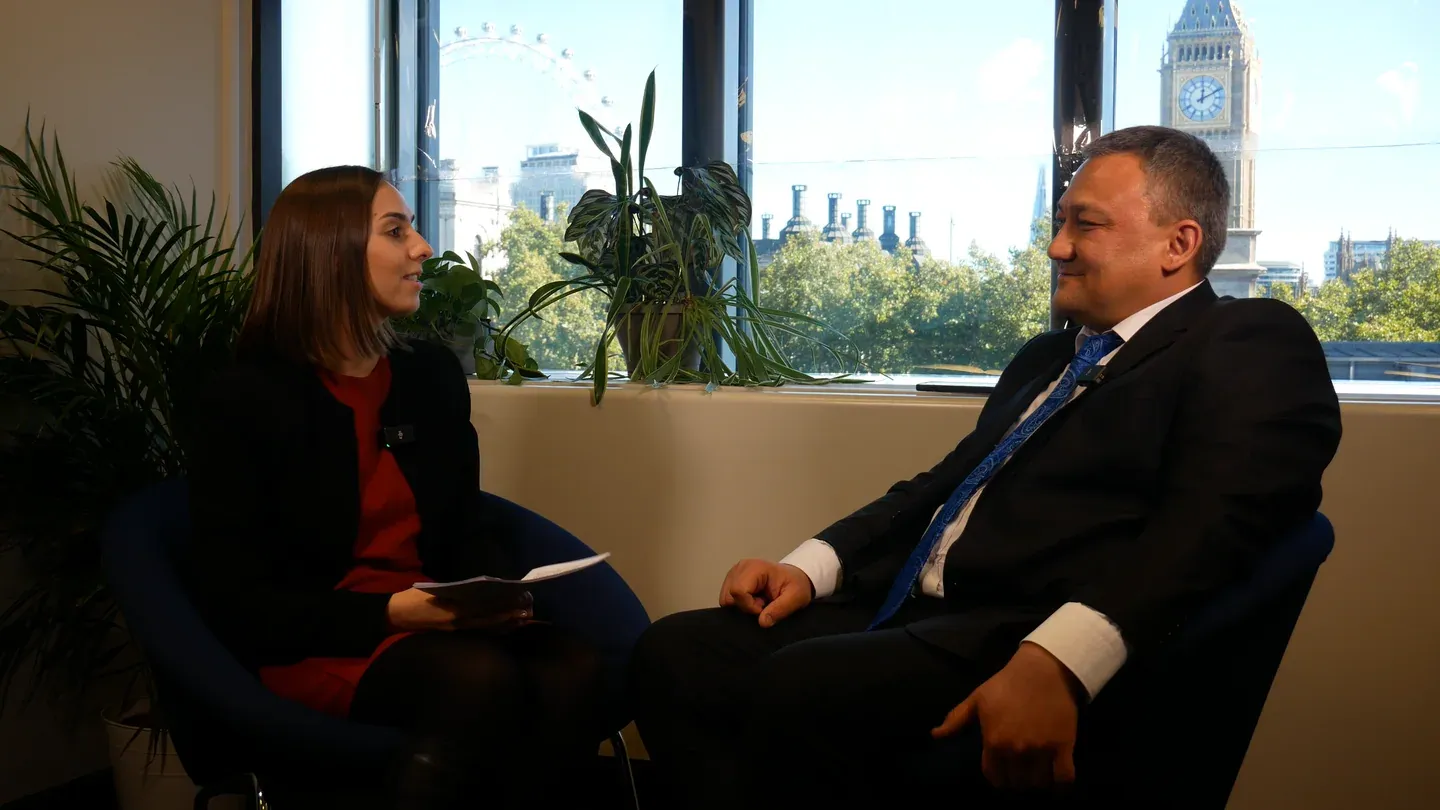 Sardor Shavkiev in a host-led IPR interview at IAMTN Summit 2026, with Westminster visible behind the speakers.